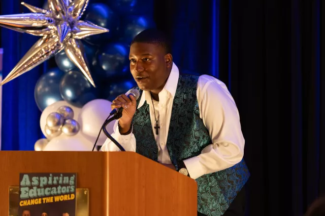 Aspiring Educators speaks into a microphone on stage.