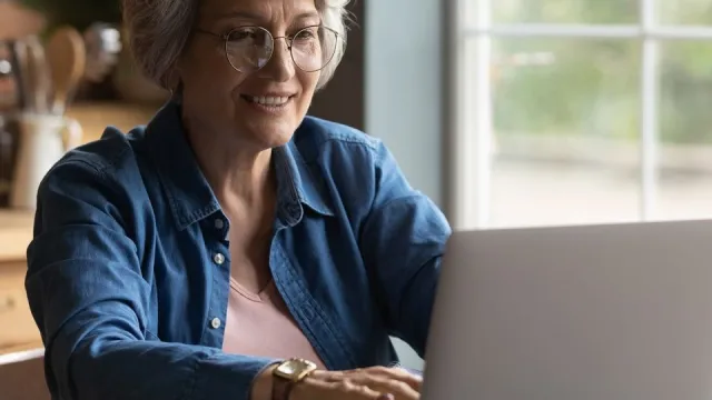 An older woman with glasses and white hair types at a computer.
