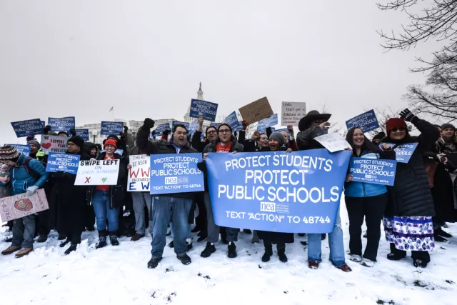 A diverse group of people stands in the snow, holding various signs that convey their messages and solidarity.