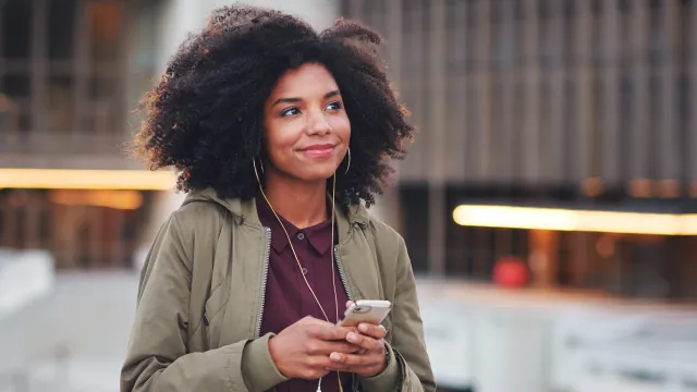 A woman smiles as she listens to something on her phone.