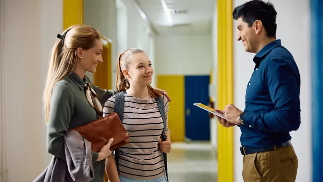 Parent, daughter, and teacher stand in the school hallway and talk