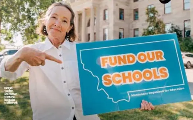 NEA member in white shirt points a sign that says Fund Our Schools