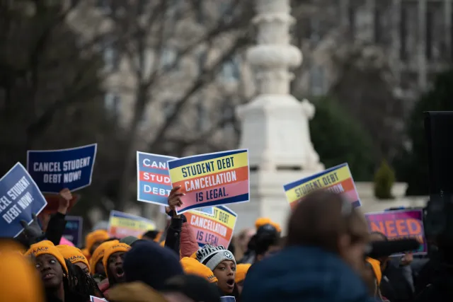Activists holding signs about cancelling student debt stand together at a rally.