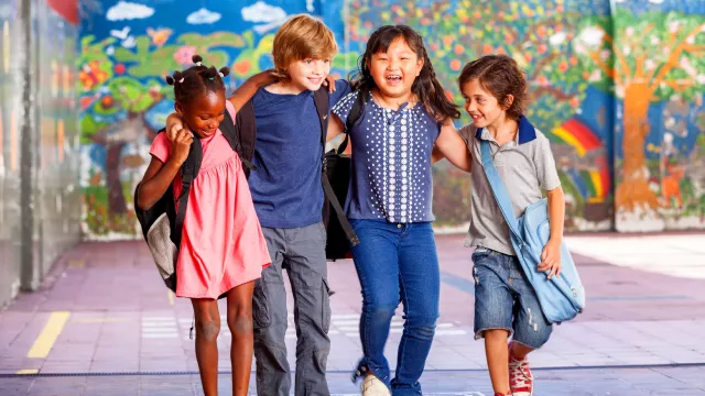 four diverse kids in elementary school lock arms with a colorful mural in the background