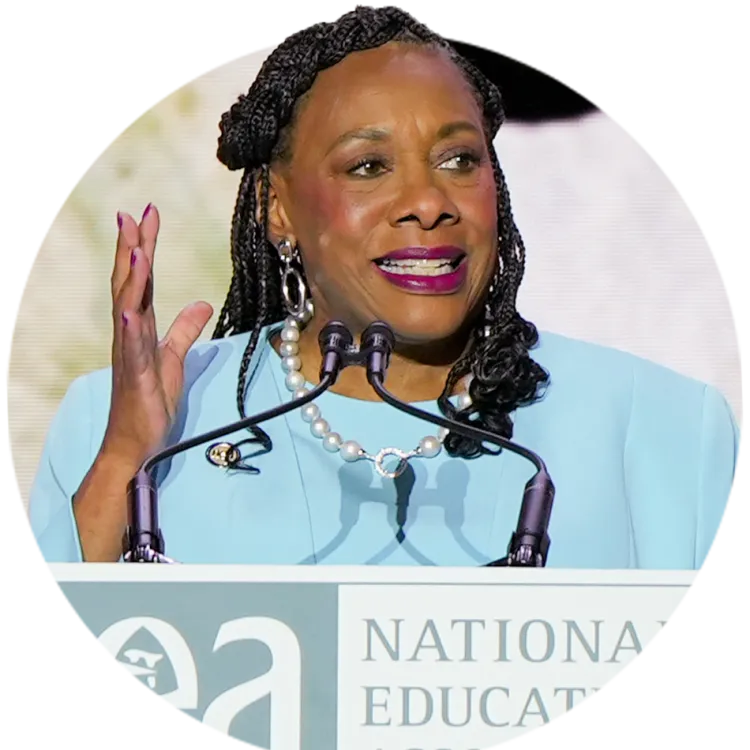 NEA President wearing an aqua colored suit stands at a lecturn and delivers her keynote address