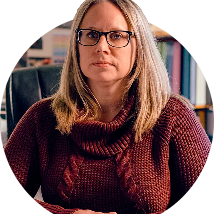 Melissa Gibbons sitting at her desk at school and looking straight into the camera, unsmiling