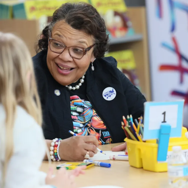 NEA Vice-President sits at a table and draws with a student at a Read Across America event