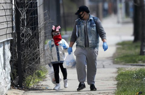 A father and child wearing masks walk hand and hand down the street