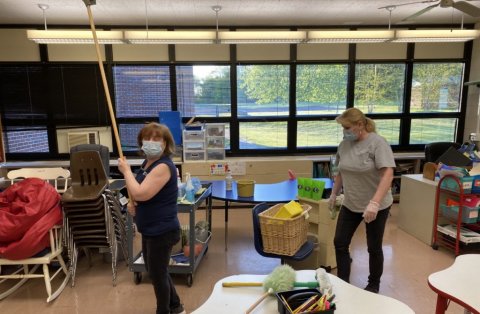 Educators wearing masks disinfect a classroom