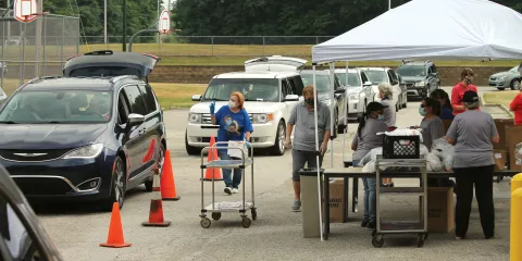 Doriann Wiegand wears a mask as she distributes food to cars lined up with their trunks open. 