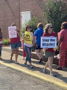 Educators with signs in front of school with signs saying "stop the attacks!"