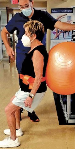Marilyn Warner balance on an exercise ball against the wall during physical therapy.