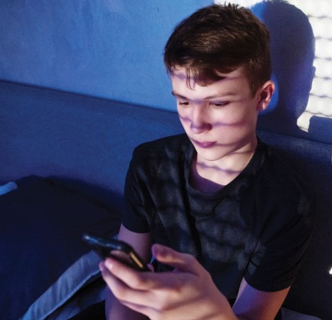 Male student on smartphone in his bedroom.