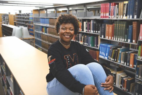 Aspiring Educator Jailyn Bridgeforth sitting on a table in a library
