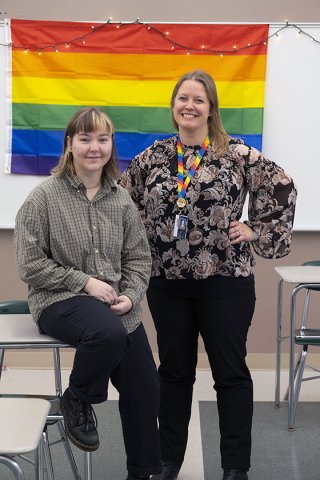 Teacher Jennifer Stefanowicz and student Rachel Fretard pose in front a rainbow flag in the classroom