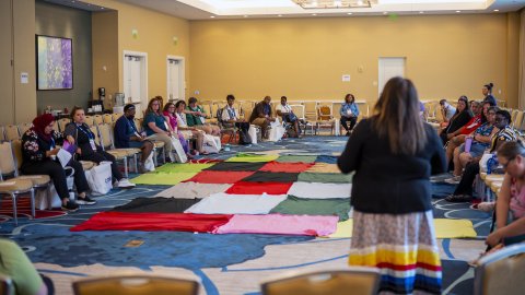 CRSJ conference attendees sit around a display of colored squares and prepare for the Blanket Exercise