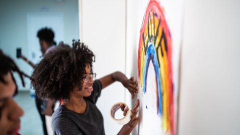 a black girl hangs a poster with a rainbow that says love on it