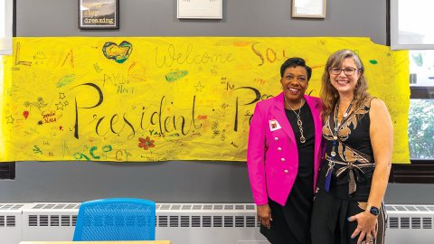 NEA President Becky Pringle stands next to teacher Karen Adkins in front of a large yellow banner with handwritten welcome messages