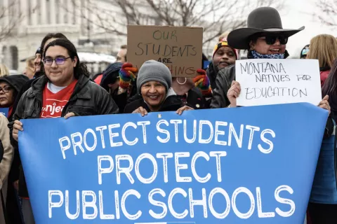 Three educators stand in front of a banner saying "protect students, protect public schools."
