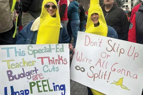 Two female protesters wearing banana costumes with various signs.