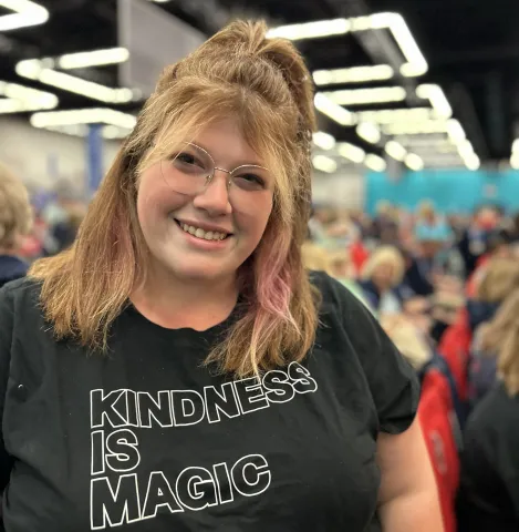 A woman smiles while wearing a "Kindness is Magic" t-shirt.
