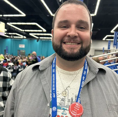 A bearded man wearing a badge on his shirt, smiling and looking directly at the camera.