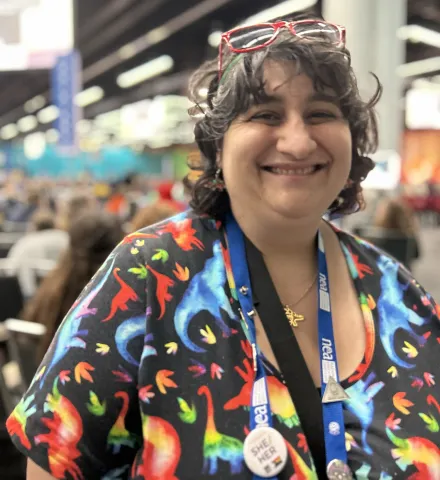 A cheerful woman wearing glasses and a vibrant shirt smiles warmly at the camera.
